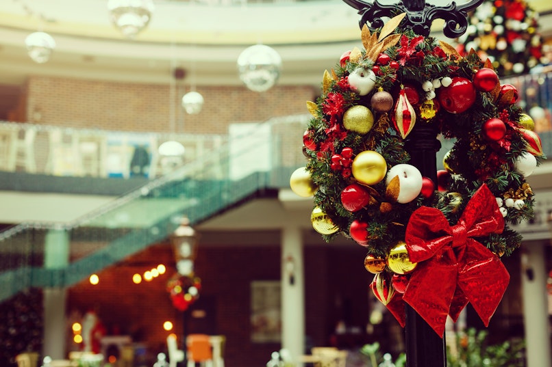 A large corporate or hotel lobby transformed with a festive commercial Christmas installation, featuring a grand decorated holiday tree and luxury botanical floral arrangements by Root Houseplants and MaryMary Florals.