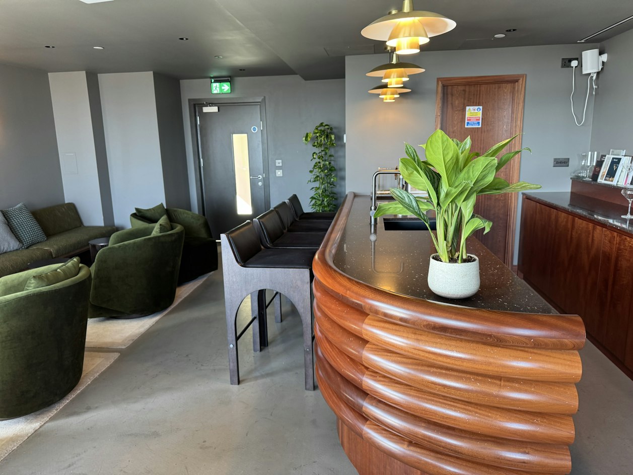 A lush indoor plant on a ribbed wooden counter in a contemporary London reception area with olive green seating.