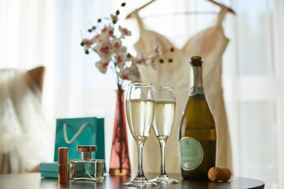 Prosecco and perfume on the table with wedding dress in the background