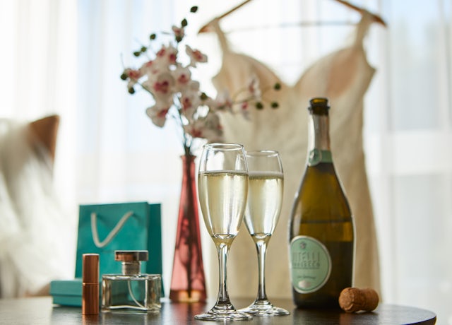 Prosecco and perfume on the table with wedding dress in the background