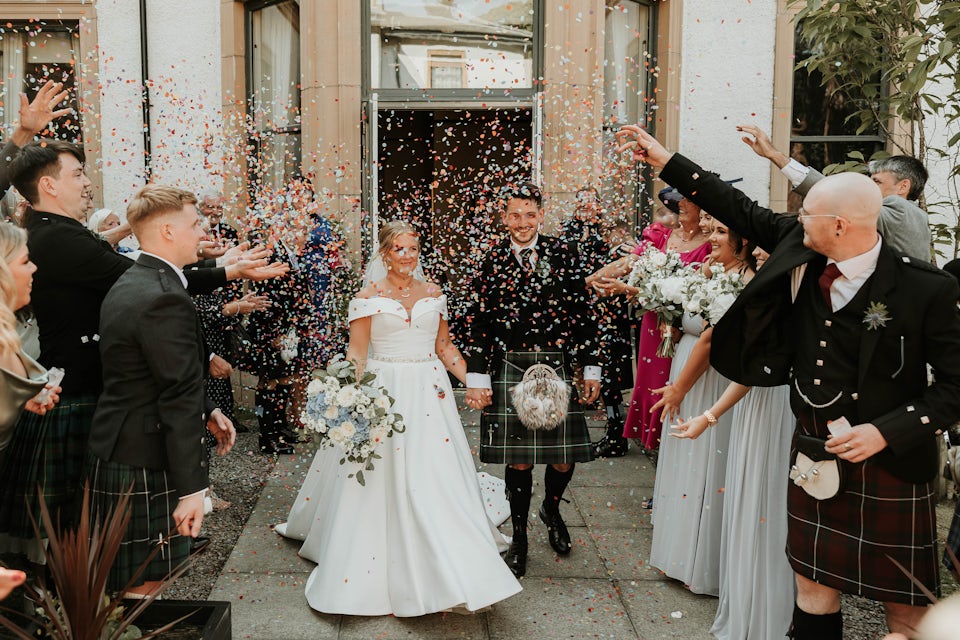 A bride and groom are showered with confetti outside Macdonald Norwood Hall