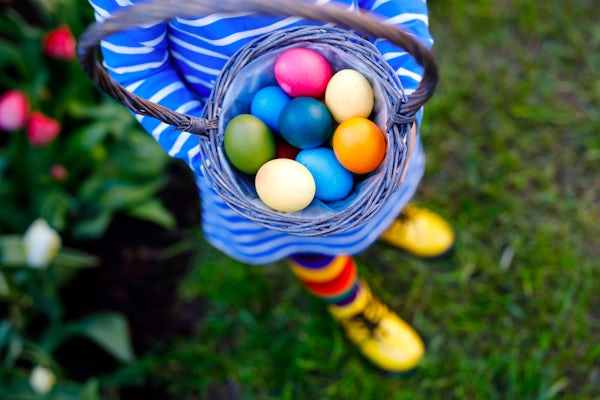 A child raises a basket of colourful Easter eggs