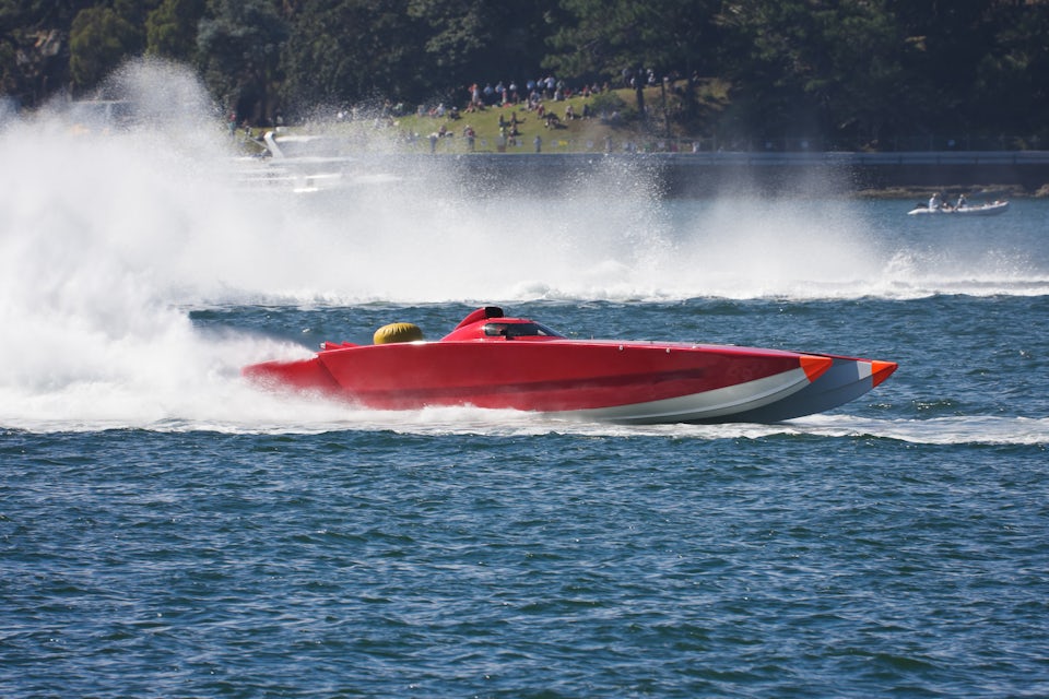 A red powerboat speeds across a lake leaving spray in its wake