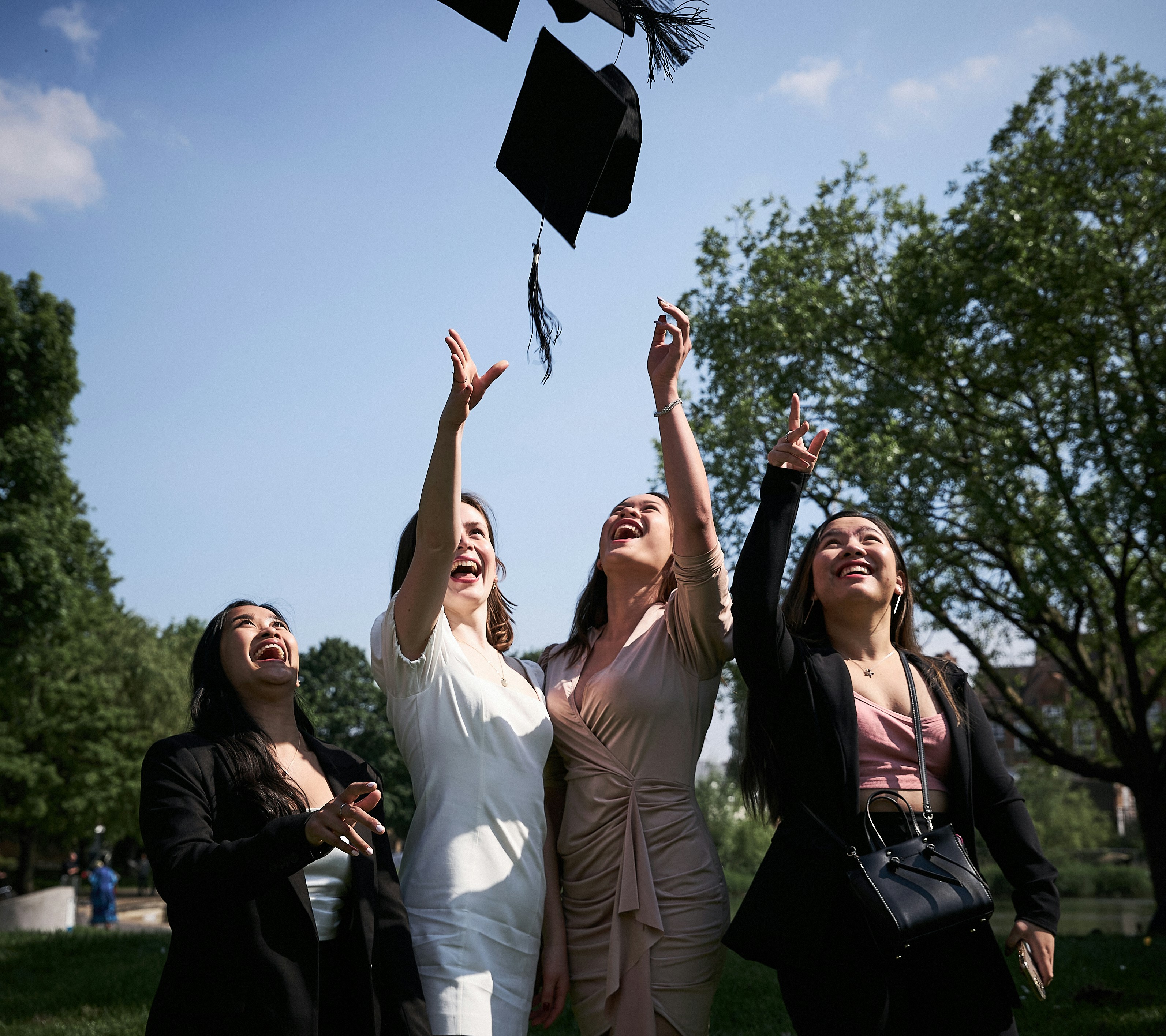 Four women throw their mortarboards into the air as they celebrate their graduation