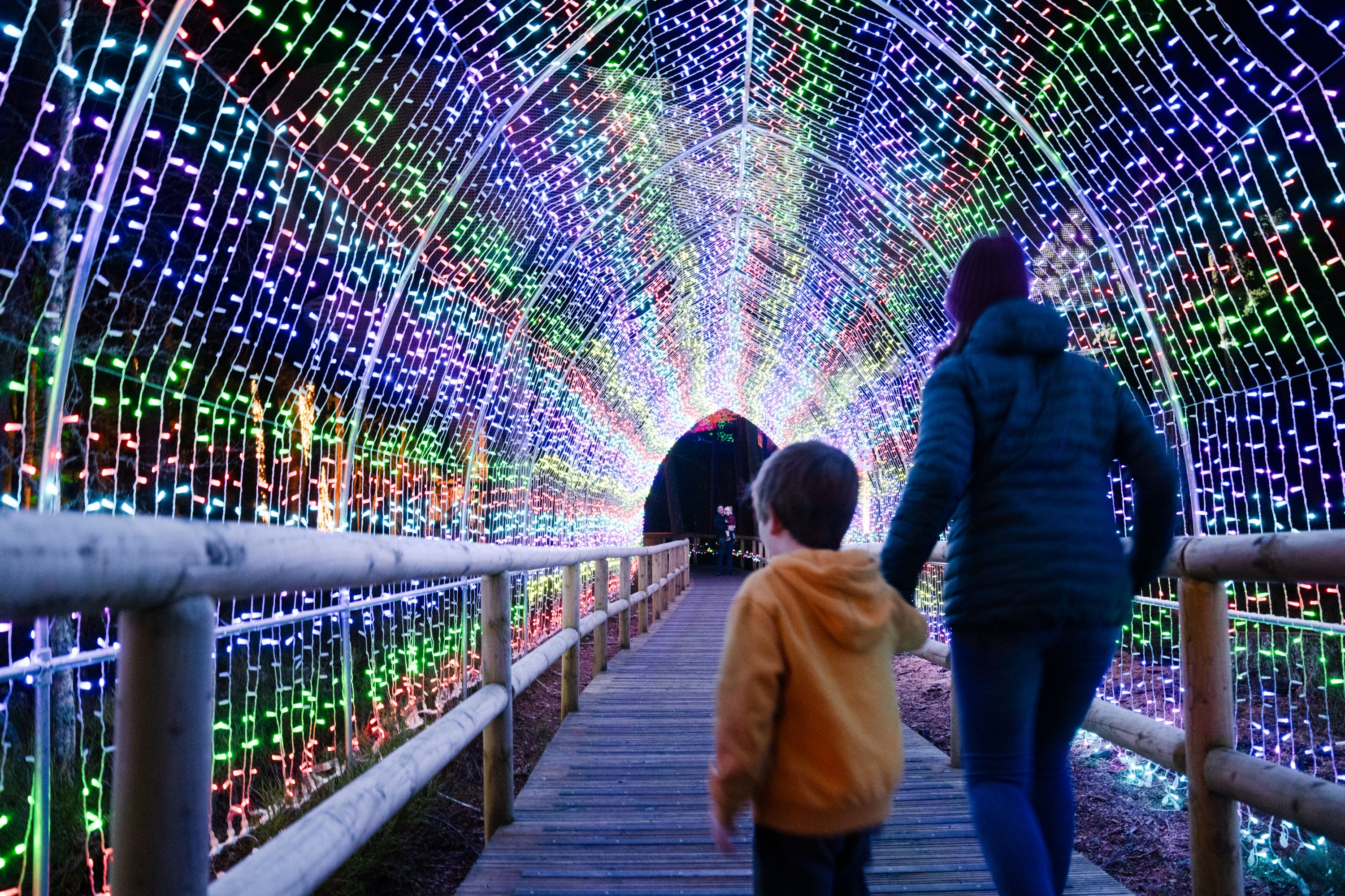 adults and child walking through tunnel made of lights