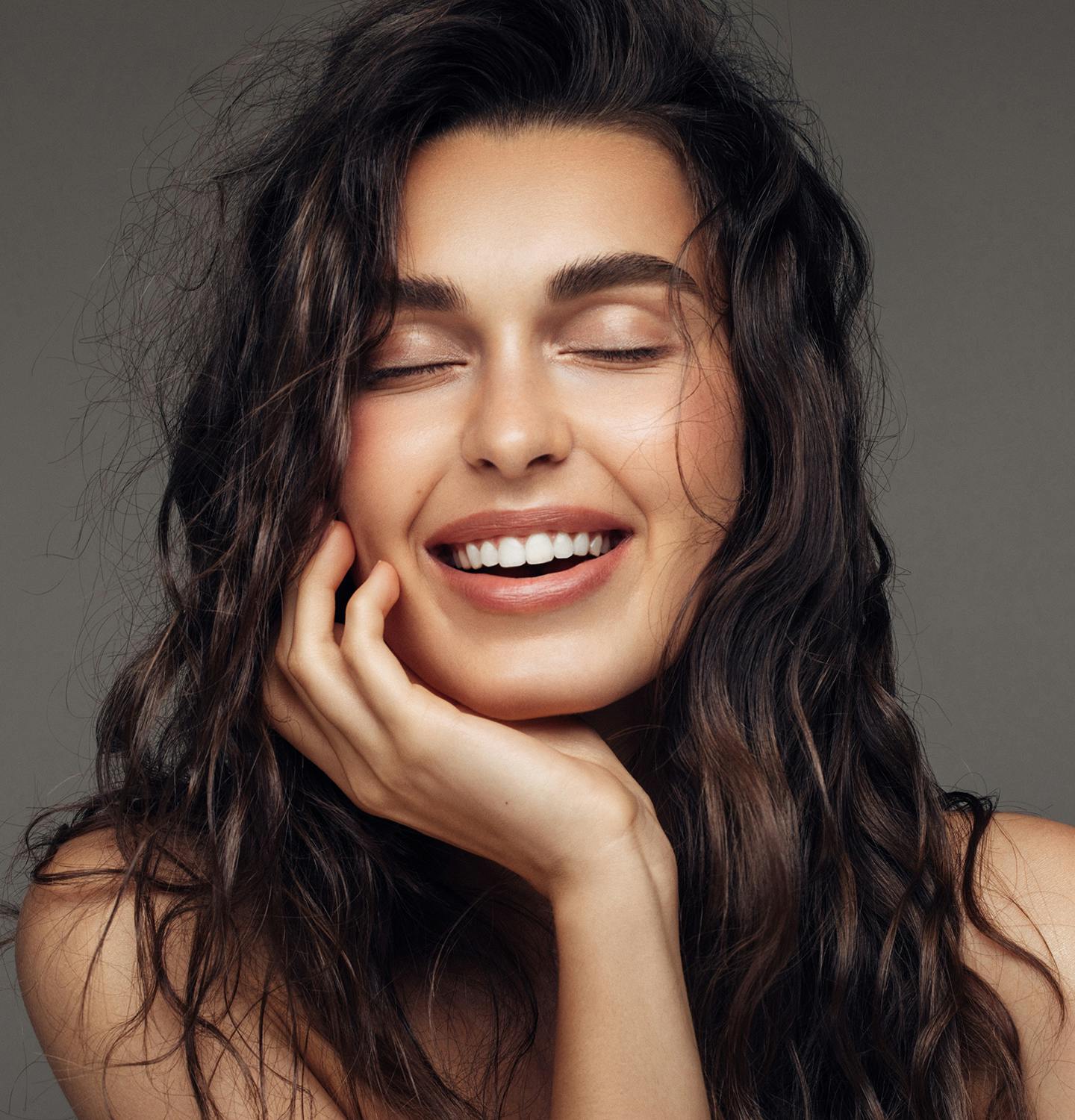 woman with long dark hair smiling and holding her hand to her face