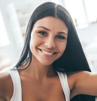 smiling woman with long black hair and white tank top posing for a picture