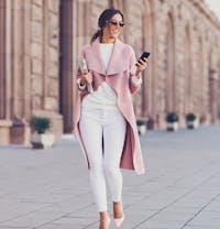 woman in a pink coat and white pants walking down a sidewalk