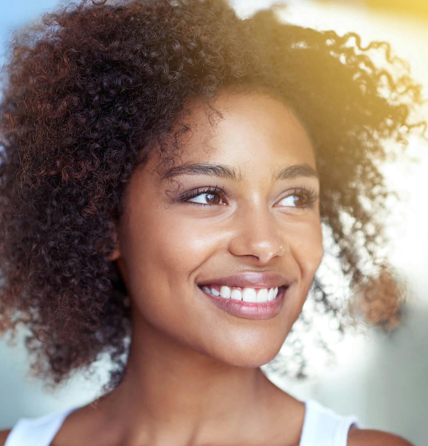 smiling woman with curly hair and white tank top looking to side