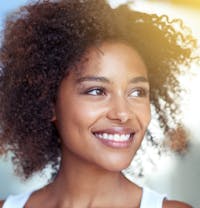 smiling woman with curly hair and white tank top looking to side