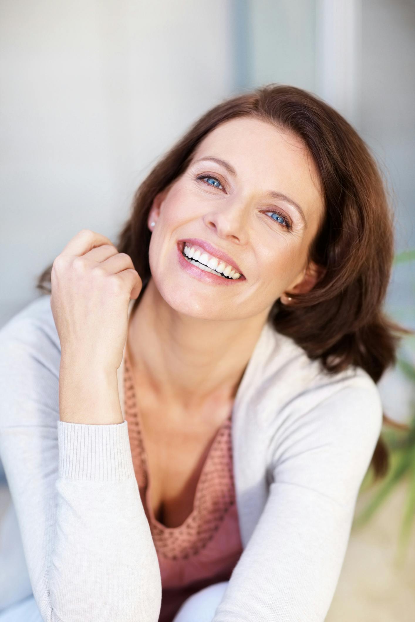 smiling woman with long brown hair and white sweater sitting on a couch