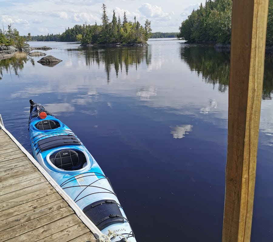 Voici la vue de la terrasse flottante de l'iloft. L'eau est calme, il fait beau et on voit des petites îles avec des grands feuillus verts. Un kayak de mer duo est accosté à la terrasse flottante. Here is the view from the floating terrace of the iloft. The water is calm, the weather is nice and we can see small islands with large green deciduous trees. A duo sea kayak is docked at the floating terrace.