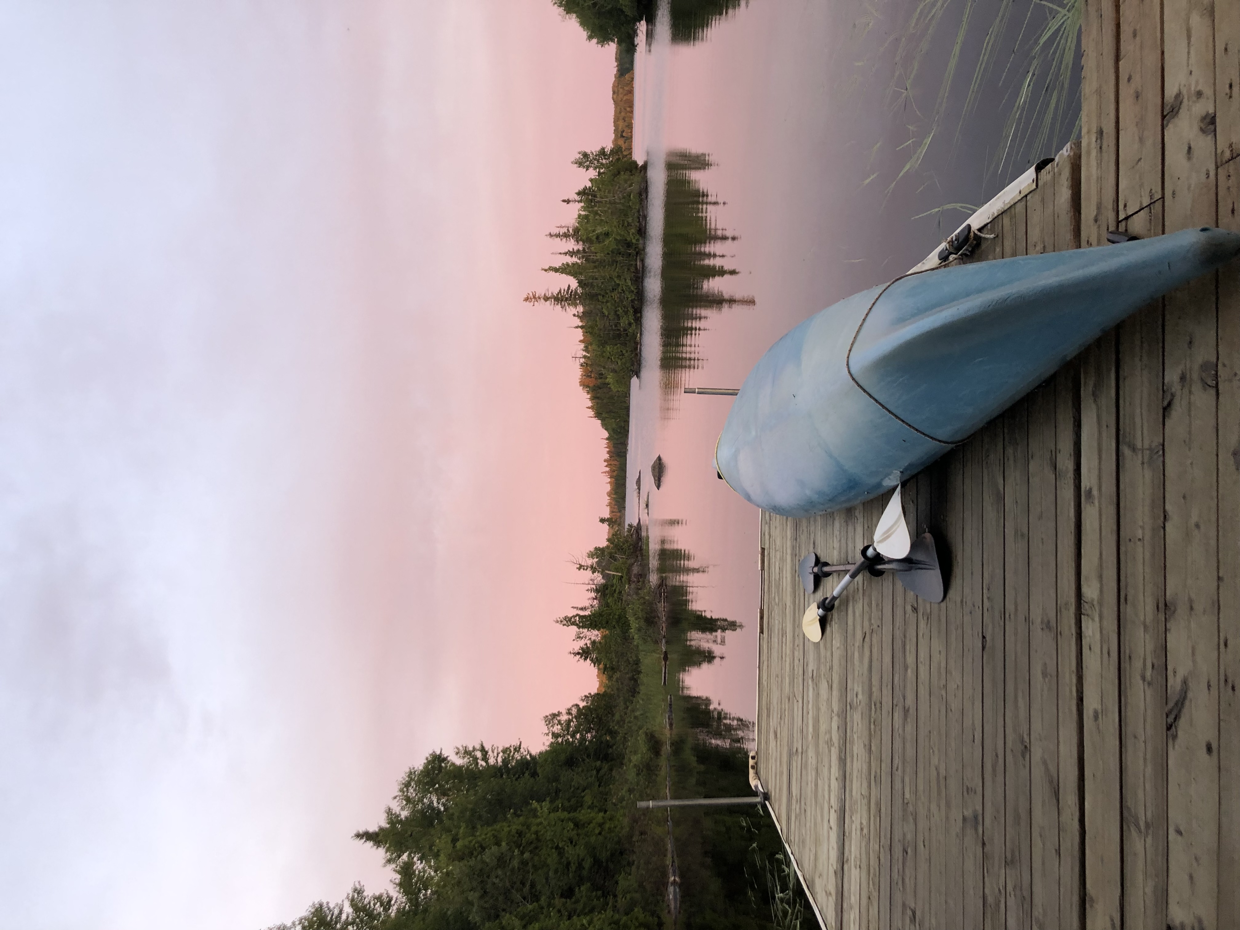 Voici la vue qu'on a sur la terrasse flottante de l'iloft au coucher du soleil. Le ciel est rose et se reflête sur le lac miroir. On voit les petites îles autour avec leurs grands feuillus verts. Un kayak est retourné sur la terrasse pour éviter que les bancs se mouiller par la rosée. Here is the view we have on the floating terrace of the iloft at sunset. The sky is pink and reflected on the mirror lake. We see the small islands around with their large green deciduous trees. A kayak is returned to the terrace to prevent the benches from getting wet with dew.