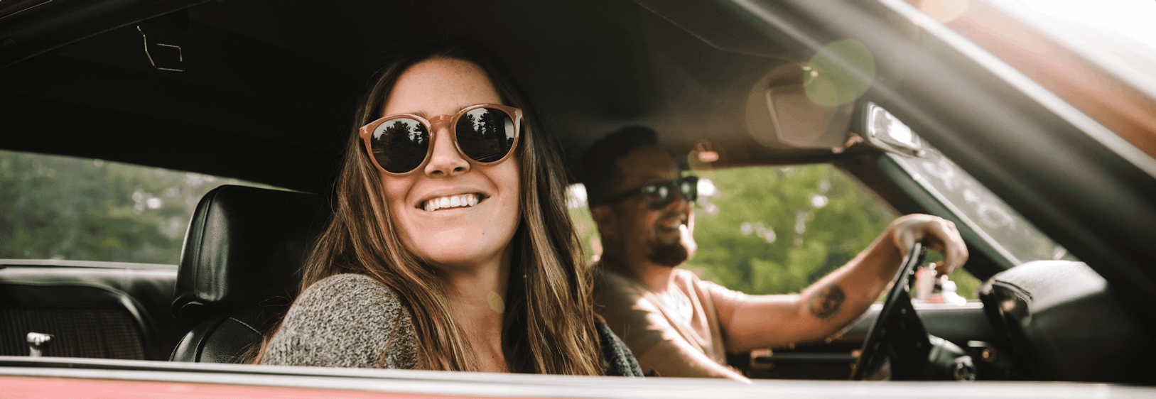 Two people site in a vintage car while smiling.