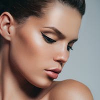 Woman looking down with winged eyeliner and hair pulled back.