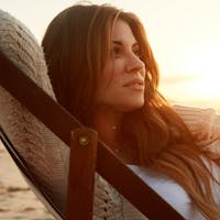 Woman laying in a lounge chair on the beach during a sunset.