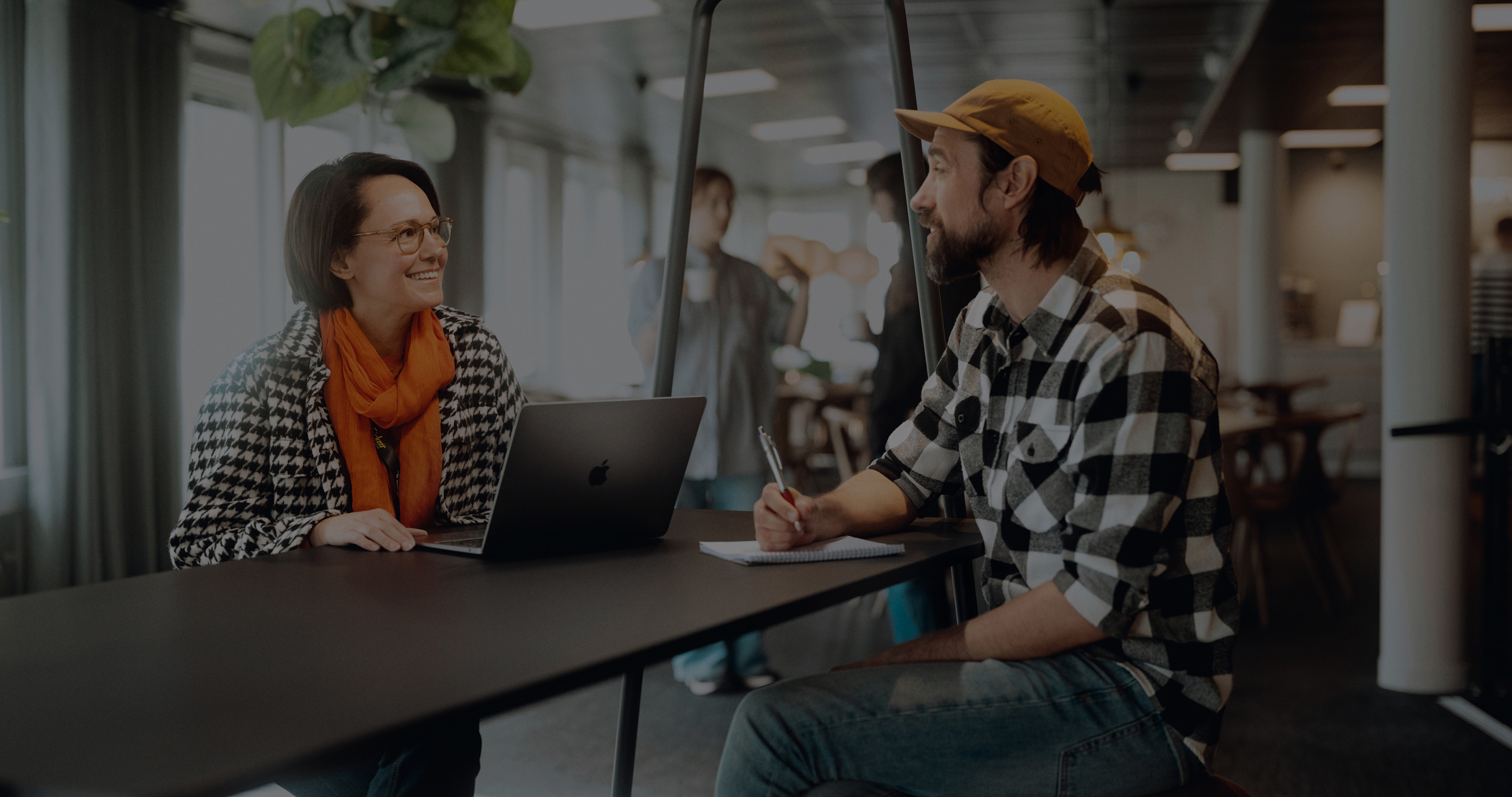 Two people sitting at a table discussing work tasks with a laptop.