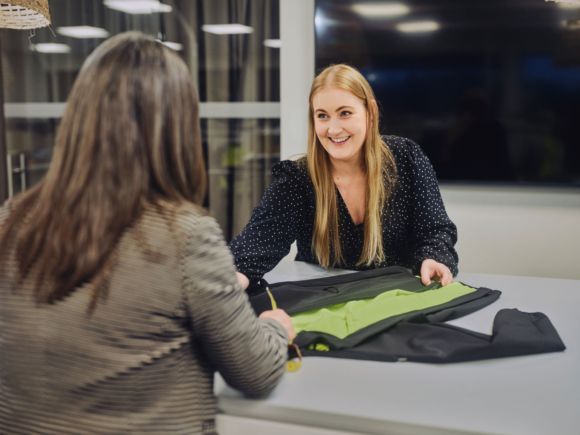 Two people reviewing a high-visibility garment laid out on a table indoors.