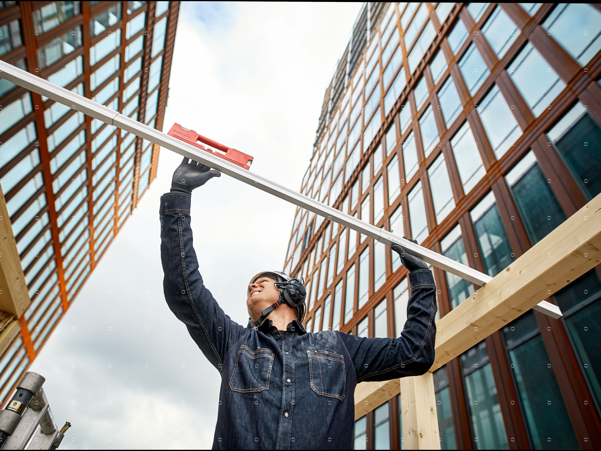 Person holding a spirit level above a wooden beam at a construction site.