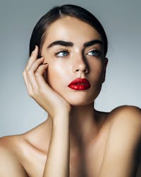 Woman with dark hair wearing red lipstick resting face on hand