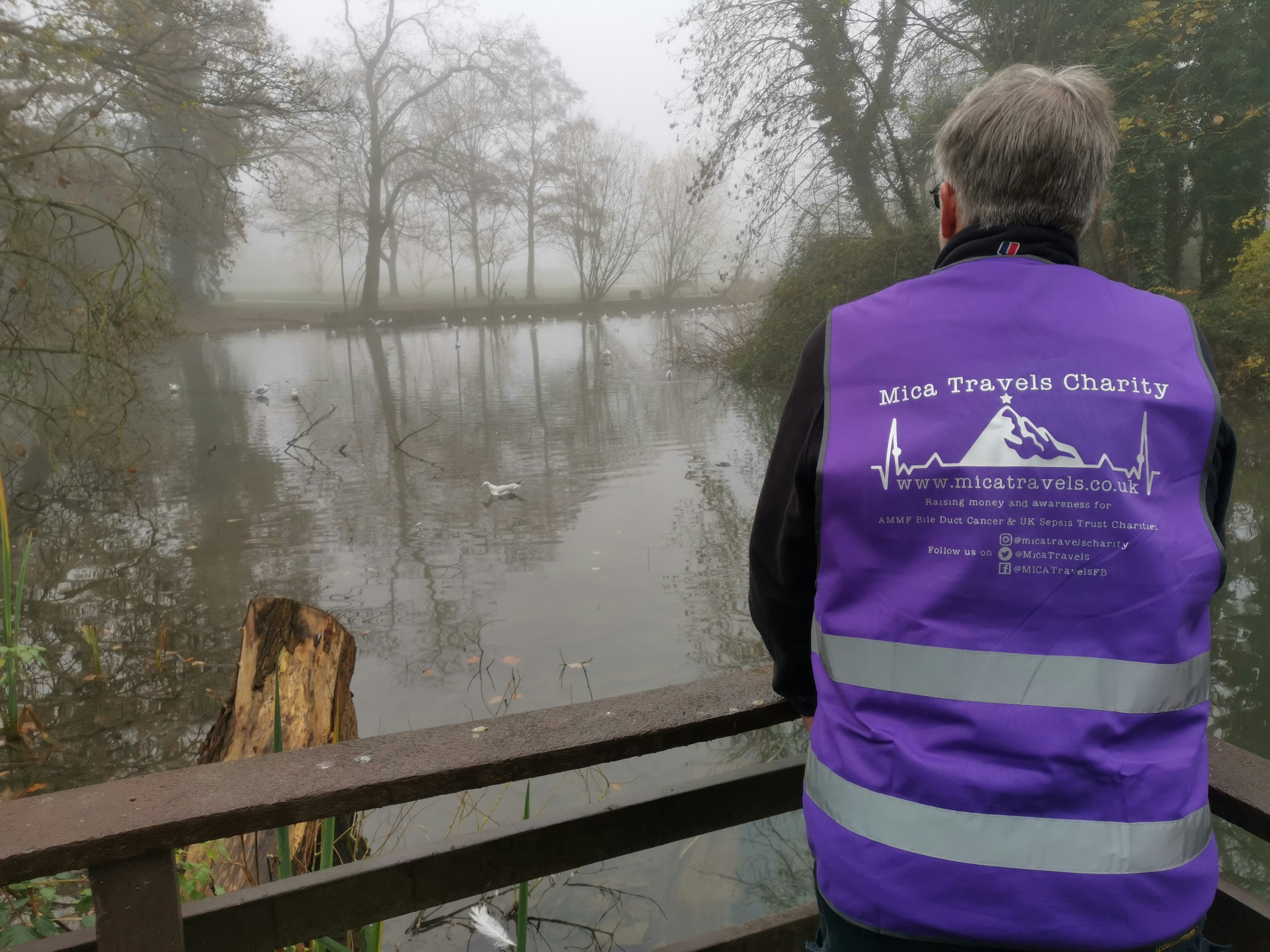 Mike looking over a misty lake in a purple reflective vest with the Mica Travels logo on