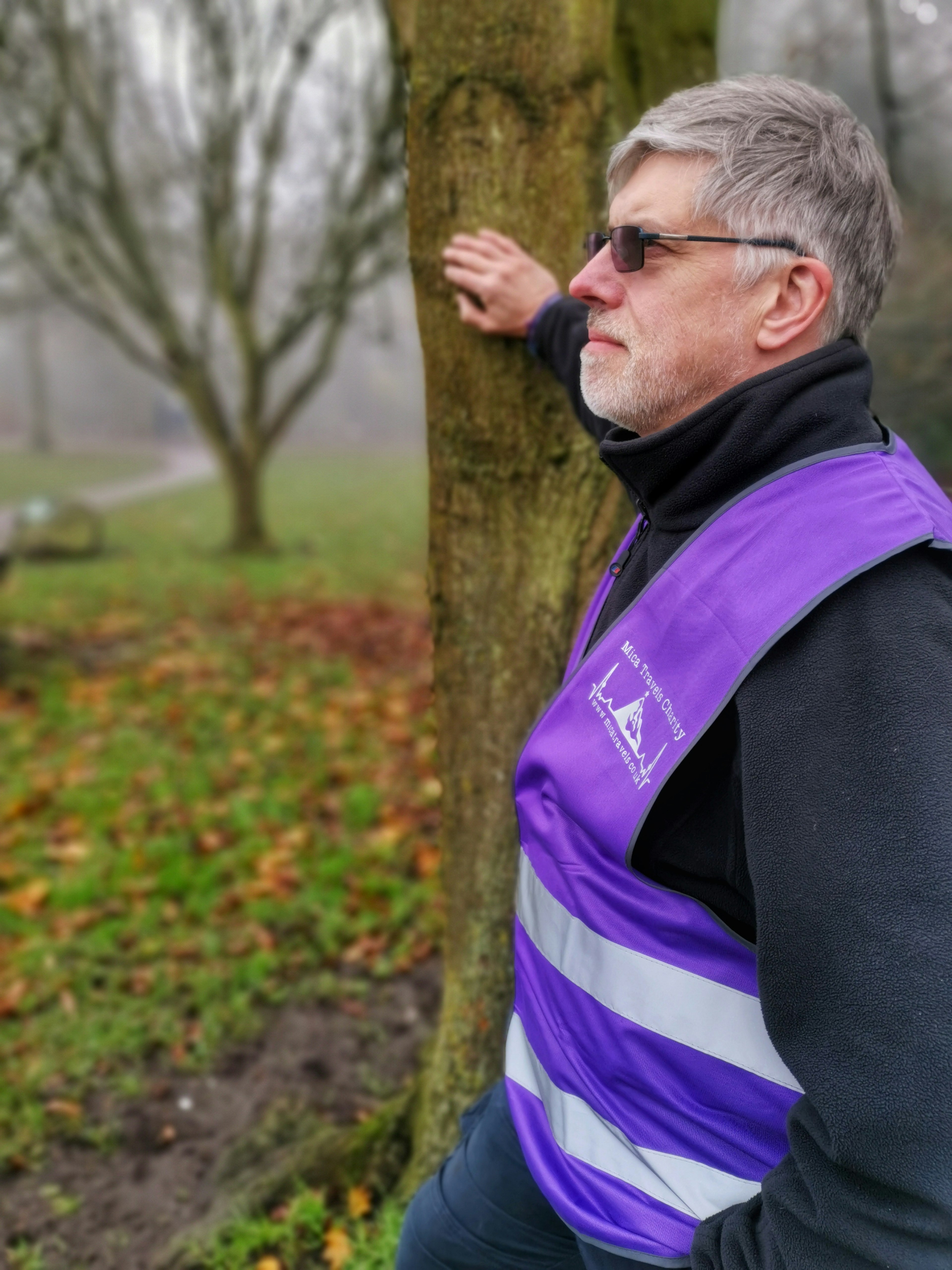 Mike leaning against a tree wearing a purple Mica Travels reflective vest