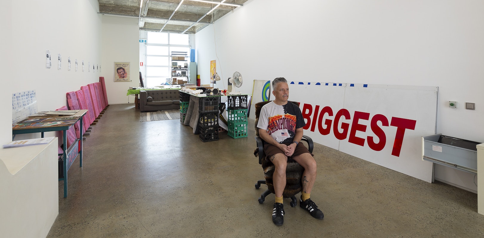 Steven Rhall, ABORIGINAL ART DISCOUNT GLASSHOUSE, installation view with the artist seated, Gertrude Glasshouse, Naarm Melbourne, 2024. Photograph: Christian Capurro