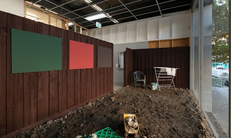 Clinton Naina, Heritage Colours, 2000/2025, installation view, 1964, 1969, 1977, 1995, 2000, 2005, 2025, Gertrude Contemporary, Naarm Melbourne, 2025, soil, drop sheet, painted timber fence, laser prints, plastic chair, heater, clothes horse, milk crate, paint, projection, image courtesy the artist and Gallerysmith, Naarm Melbourne © the artist, photograph: Christian Capurro.