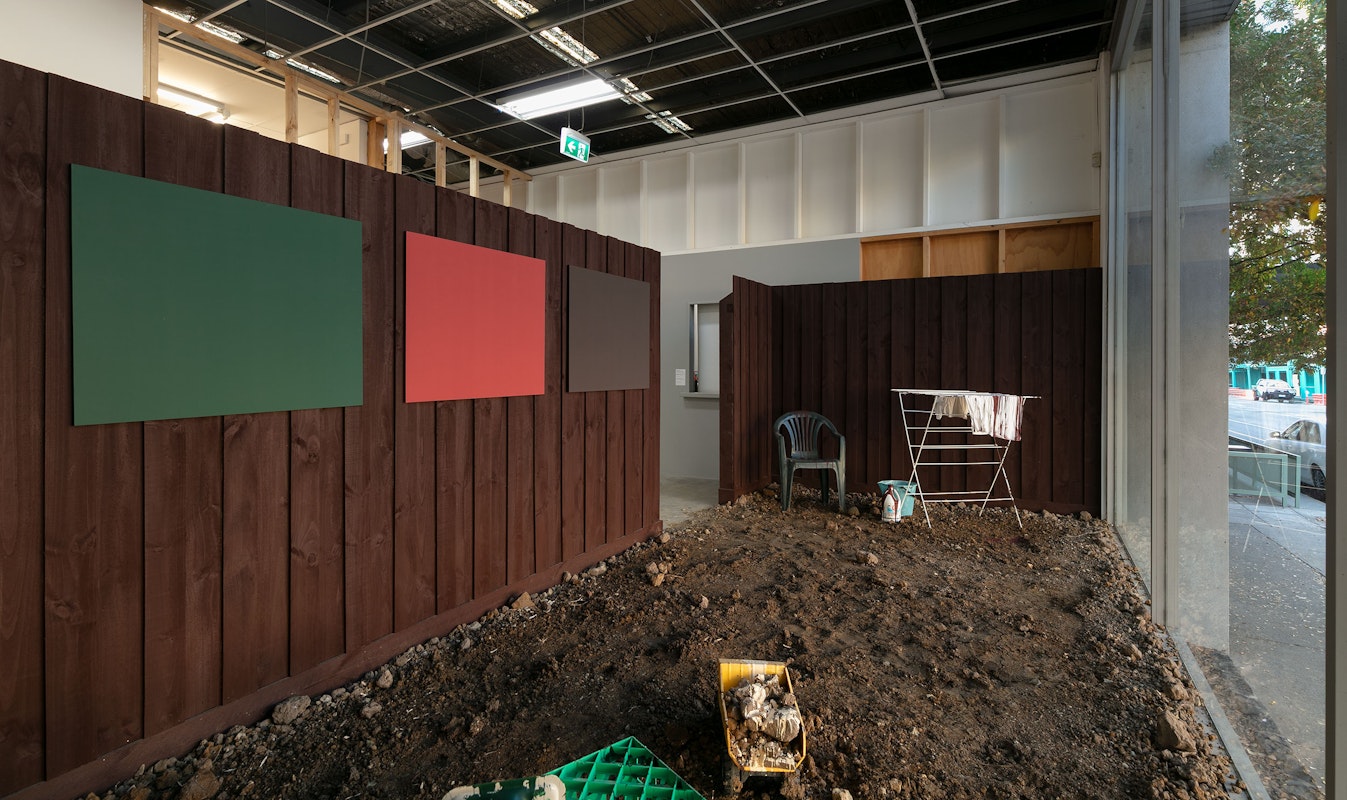 Clinton Naina, Heritage Colours, 2000/2025, installation view, 1964, 1969, 1977, 1995, 2000, 2005, 2025, Gertrude Contemporary, Naarm Melbourne, 2025, soil, drop sheet, painted timber fence, laser prints, plastic chair, heater, clothes horse, milk crate, paint, projection, image courtesy the artist and Gallerysmith, Naarm Melbourne © the artist, photograph: Christian Capurro.