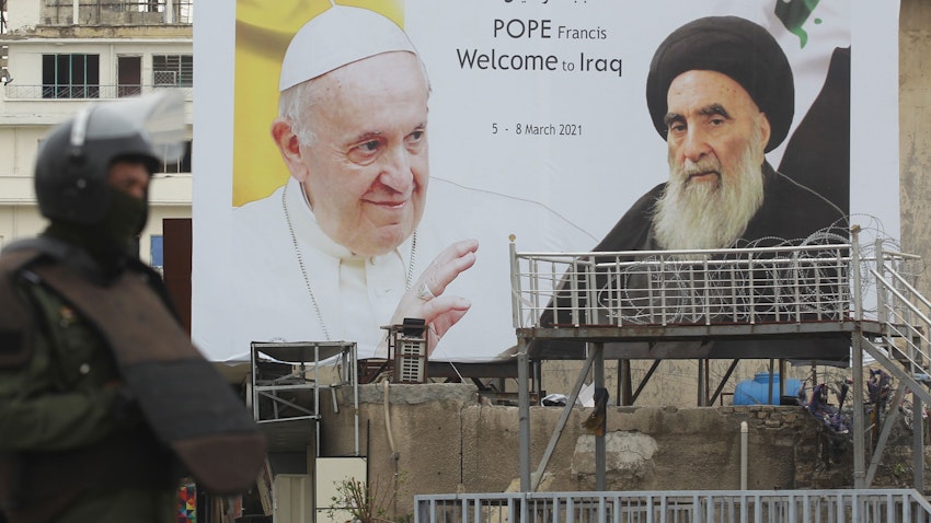 حارس أمن عراقي يقف أمام لوحة إعلانية تحمل صور البابا وآية الله علي السيستاني وسط بغداد، 4 مارس/آذار 2021 (الصورة عبر غيتي إيماجز)
