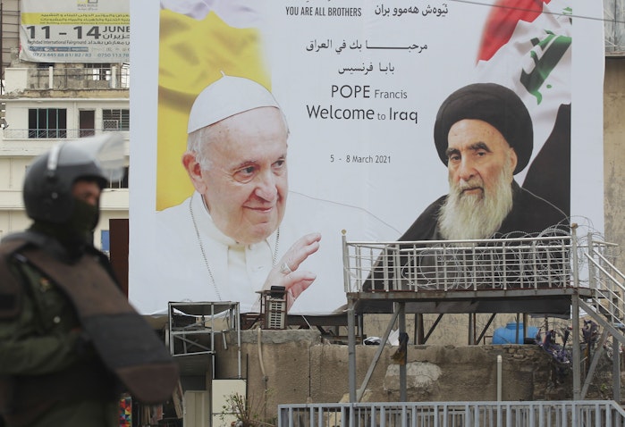 An Iraqi security guard stands in front of a billboard bearing portraits of the Pope and Ayatollah Ali Sistani in central Baghdad on March 4, 2021. (Photo via Getty Images)