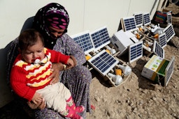 إمرأة نازحة مع حفيدها يجلسان بجوار ألواح الطاقة الشمسية في مخيم للاجئين في أربيل، العراق في 1 فبراير/شباط، 2015. (الصورة عبر غيتي إيماجز)