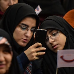Two Iranian students look at a cellphone during a summit in Allame Tabatabi University. Tehran, Iran. Dec. 7, 2019. (Photo by Behnam Tofiqi Forouhar via Mehr News Agency)