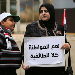 یک زن عراقی در تظاهرات ضد فساد با پلاکاردی که روی آن نوشته شده است "آری به شهروندی، نه به فرقه‌گرایی"؛ بغداد، ۲ بهمن ۱۳۹۴/ ۲۲ ژانویه ۲۰۱۶. (عکس از گتی ایمیجز)