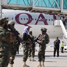 Taliban fighters stand guard as passengers board a Qatar Airways plane at the airport in Kabul, Afghanistan, on Sept. 14, 2021. (Photo via Getty Images)