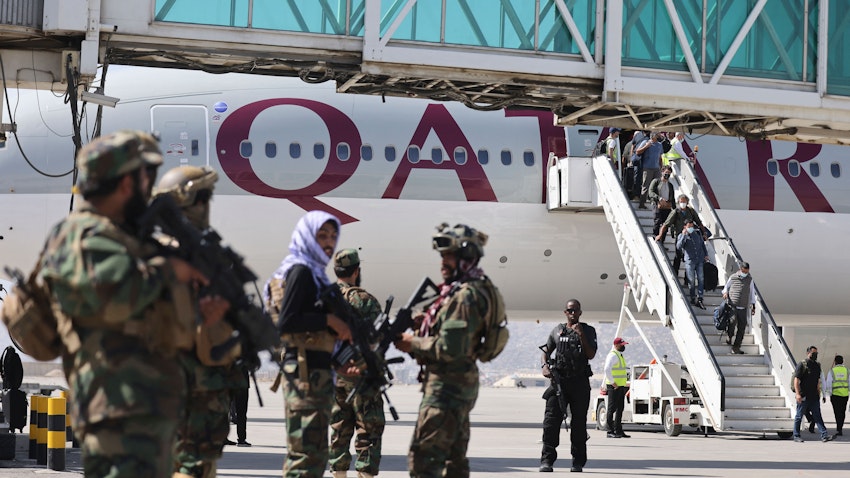 Taliban fighters stand guard as passengers board a Qatar Airways plane at the airport in Kabul, Afghanistan, on Sept. 14, 2021. (Photo via Getty Images)