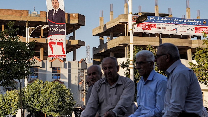 Men sit together while displayed on a nearby building is an electoral banner for the Oct. 10 parliamentary elections in Zakho, Iraq on Oct. 5, 2021. (Photo via Getty Images)