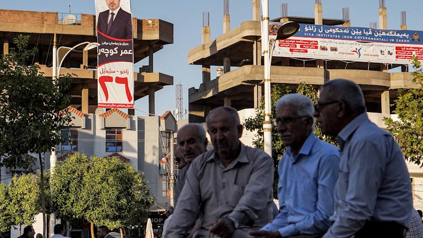 چند مرد، نشسته در نزدیکی ساختمانی که بنر تبلیغاتی انتخابات پارلمانی ۲۸ مهر/ ۱۰ اکتبر بر روی آن نصب شده است؛ زاخو، ۱۳ مهر ۱۴۰۰/ ۵ اکتبر ۲۰۲۱. (عکس از گتی ایمیجز)