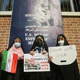 سه زن ایرانی با بنرهای ضدامریکایی  در مقابل سفارت سابق آمریکا در تهران؛ ۱۳  آبان ۱۴۰۰. (عکس از حسین ظهروند/  خبرگزاری تسنیم) 