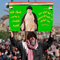 تصویر روحانی شیعه، مقتدی صدر، در دستان مردی عراقی در نمازجمعه‌؛ بغداد، ۱۲ آذر ۱۴۰۰/ ۳ دسامبر ۲۰۲۱. (عکس از گتی ایمیجز)