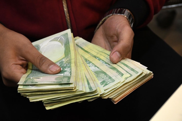 An employee of a currency exchange counter shows a stack of Iraqi dinars in Nasiriyah, Iraq on Dec. 20, 2020. (Photo via Getty Images)