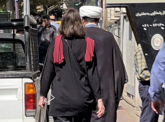 A cleric and a woman without a head scarf walking in the heart of the Iranian capital Tehran, on Oct. 11, 2022. (Photo via Getty Images)