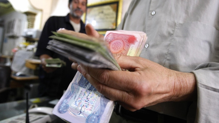 An Iraqi man counts out Iraqi Dinars at a money changer in central Baghdad, on May 25, 2009. (Photo via Getty Images)