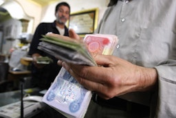 An Iraqi man counts out Iraqi Dinars at a money changer in central Baghdad, on May 25, 2009. (Photo via Getty Images)