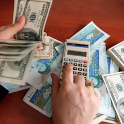 تاجر إيراني يعد أوراق نقدية من فئة الـ 100 دولار أميركي والريال الإيراني في مكتب صرافة عملات في طهران، إيران في 22 ديسمبر/كانون الأول 2010. (الصورة عبر غيتي إيماجز)