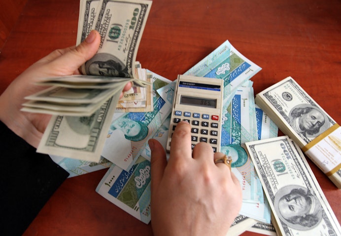 An Iranian dealer counts US 100-dollar bills and Iran's rial banknotes in a currency exchange office in Tehran on Dec. 22, 2010. (Photo via Getty Images)