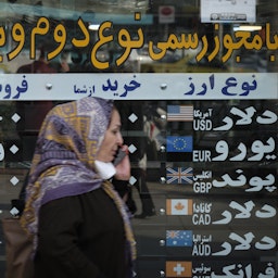 یک زن ایرانی در حال عبور از جلوی یک صرافی در منطقه‌ی تجاری تهران، ۱۹ مهر ۱۳۹۹. (عکس از طریق گتی ایمیجز)