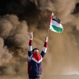 A Palestinian man raises a flag during clashes with Israeli forces near the Israel-Gaza border, east of Gaza City on Jan. 26, 2023. (Photo via Getty Images)