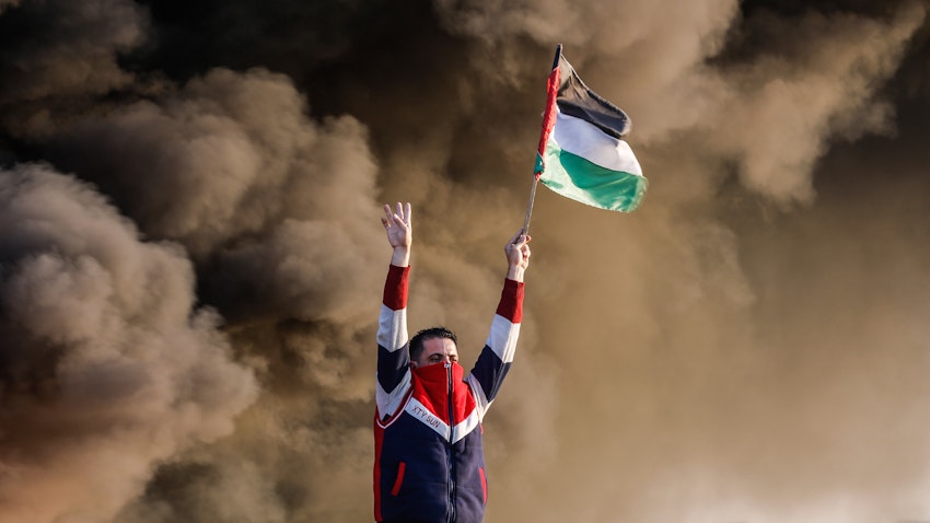 A Palestinian man raises a flag during clashes with Israeli forces near the Israel-Gaza border, east of Gaza City on Jan. 26, 2023. (Photo via Getty Images)