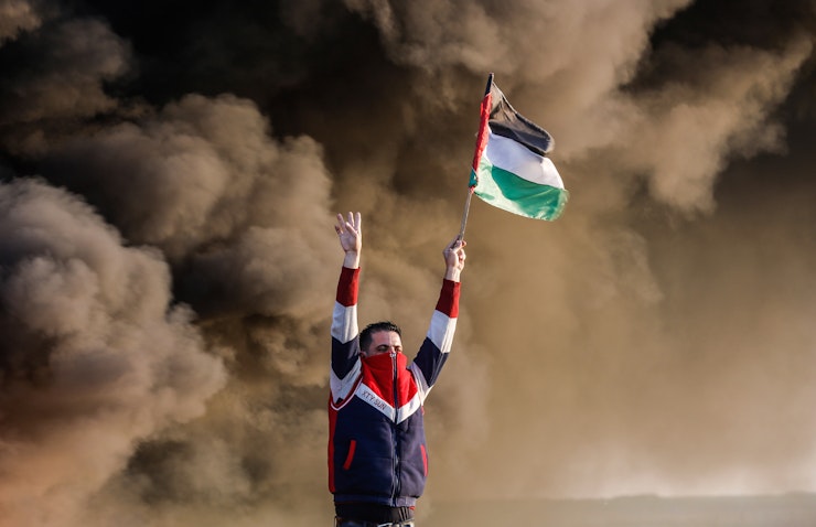 پرچمی در دست یک مرد فلسطینی، در جریان درگیری با نیروهای اسرائیلی در نزدیکی مرز اسرائیل و غزه؛ شرق شهر غزه، ۶ بهمن ۱۴۰۱. (عکس از گتی ایمیجز)